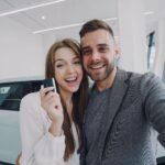 Młoda para robi selfie przy nowo kupionym samochodzie w salonie