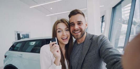 Młoda para robi selfie przy nowo kupionym samochodzie w salonie