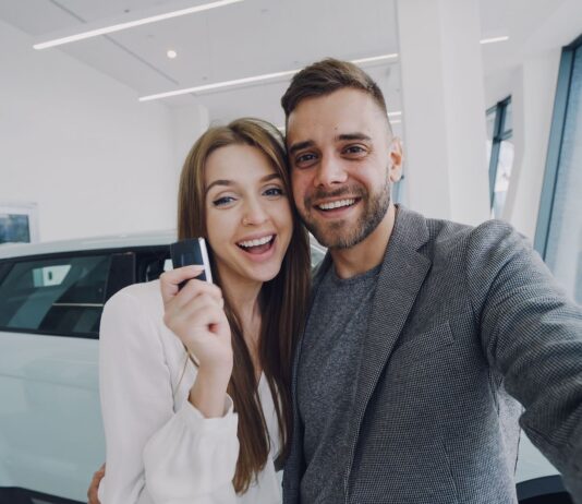 Młoda para robi selfie przy nowo kupionym samochodzie w salonie