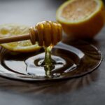 Miód spływający z drewnianej łyżki do spodeczka z cytryną